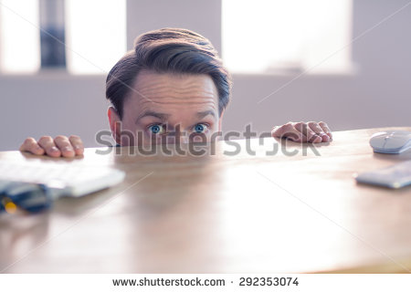 stock-photo-nervous-businessman-peeking-over-desk-in-his-office-292353074