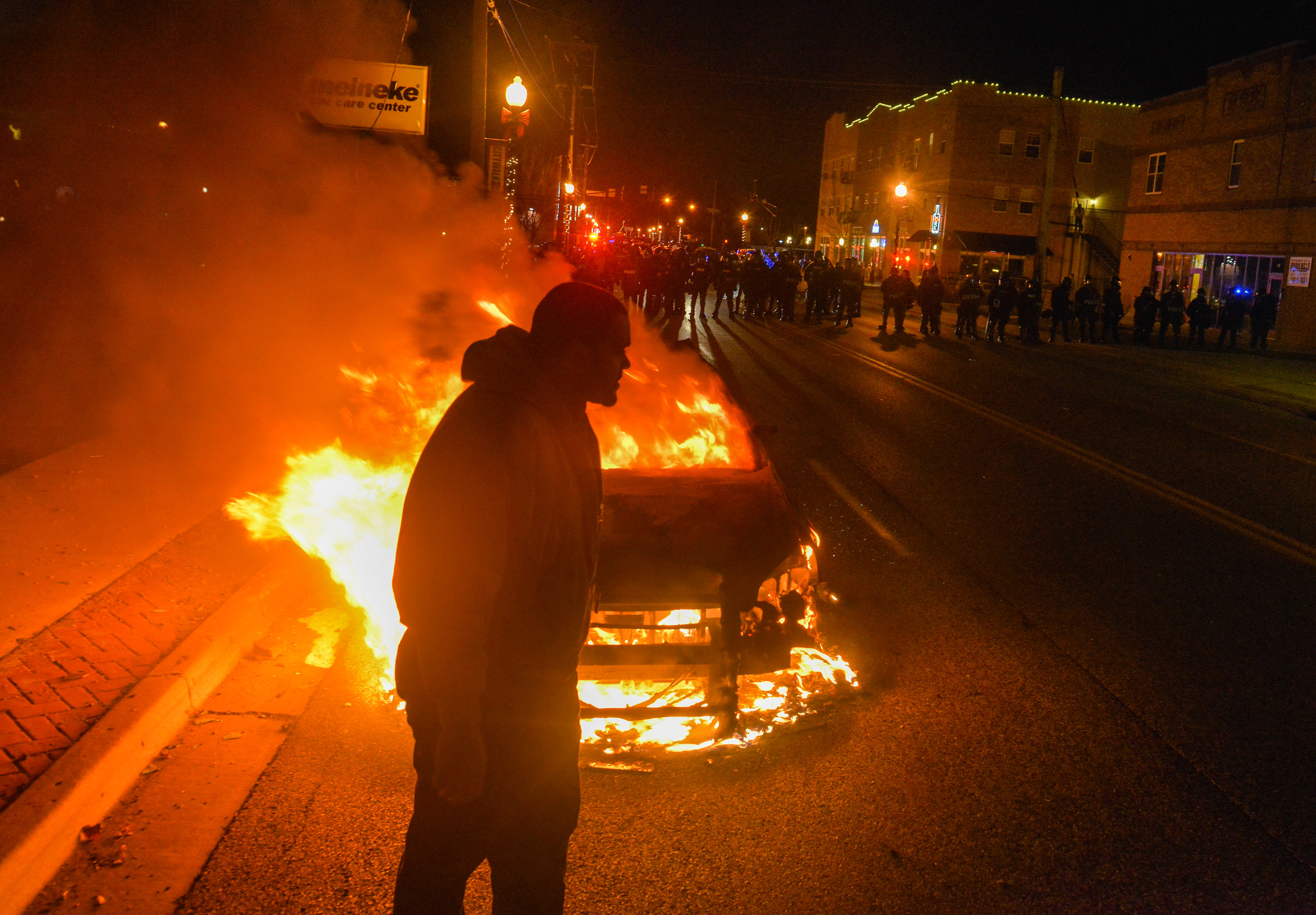 FERGUSON, MO - NOVEMBER 24: A man makes his way past a burning police car as a line of officers prepare to clear the street of protesters after an announcement that Ferguson police officer Darren Wilson will not be indicted in the fatal shooting of unarmed teenager Michael Brown, on Monday, November 24, 2014, in Ferguson, MO.  The shooting of Michael Brown, an unarmed black 18-year-old by white Ferguson police officer Darren Wilson, has captivated the nation as a grand jury deliberated to decide whether to charge the officer with a crime.   (Photo by Jahi Chikwendiu/The Washington Post)