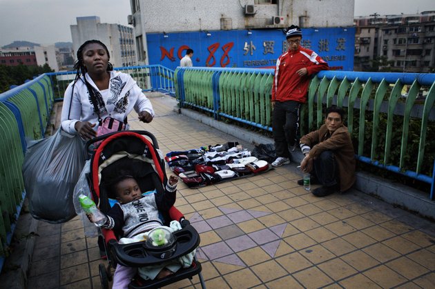 GUANGZHOU, CHINA - DECEMBER 13:  An African woman with a baby in a stroller pass a pedestrian bridge where Chinese street vendors aretrying to attract customers December 13, 2008 in Guangzhou, China. In Guangzhou, the largest city in south China, 20.000 Africans are trying to make a life for themselves as traders in wholesale markets. Here, they hope to carve out their own piece of the Chinese economical miracle. The traders buy clothes and other cheap goods to be shipped and sold back home. Approximately 80% of the Africans in Guangzhou are Nigerians, others are from e.g. Ghana, Kenya and Cameroon.  (Photo by David Hogsholt/Getty Images)